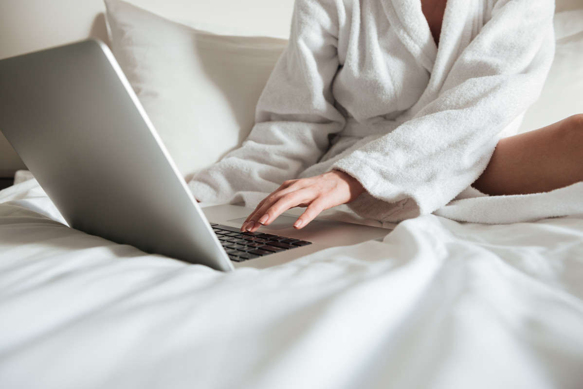Mujer en bata de bano en la cama y usando laptop