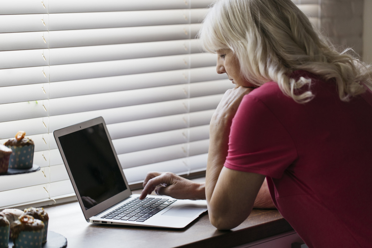 Mujer madura que usa la computadora portatil cerca de la ventana